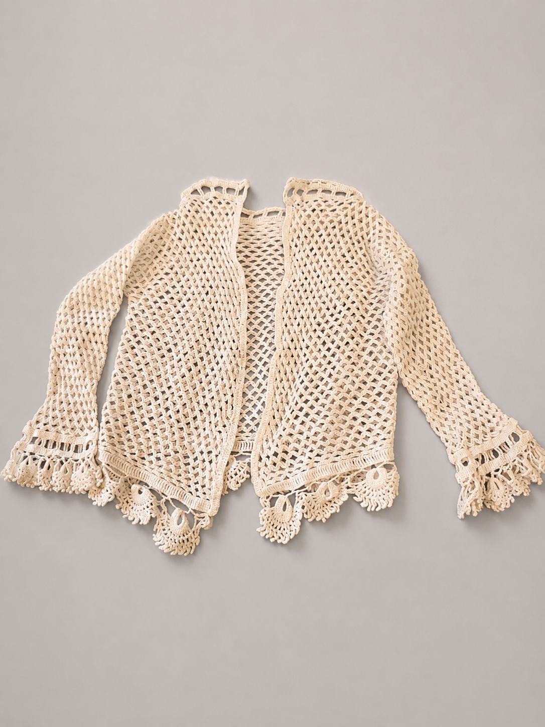 Vintage 1940s hand-crocheted cream/beige tiny cardigan, with a delicate openwork pattern, ruffled cuffs, and decorative fan-shaped edging.